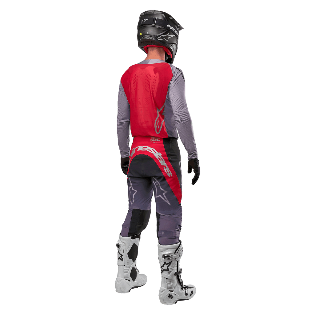Alpinestars 2024 Supertech Dade Jersey, koszulka motocrossowa, kolor Iron Red Berry i szary, widok z tyłu na motocykliście, czerwony panel tylny z szarym logo i szarymi rękawami, noszona z dopasowanymi szaro-czerwonymi spodniami wyścigowymi, białymi butami i czarnym kaskiem, profesjonalna odzież off-road.