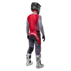 Alpinestars 2024 Supertech Dade Jersey, koszulka motocrossowa, kolor Iron Red Berry i szary, widok z tyłu na motocykliście, czerwony panel tylny z szarym logo i szarymi rękawami, noszona z dopasowanymi szaro-czerwonymi spodniami wyścigowymi, białymi butami i czarnym kaskiem, profesjonalna odzież off-road.