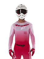 Zawodnik motocrossowy w koszulce Alpinestars 2024 Supertech Dade w kolorze Red Berry Lilac, pasujące spodnie, biały kask z czarnymi goglami i czerwone rękawice, profesjonalny strój wyścigowy z gradientem różu i czerwieni