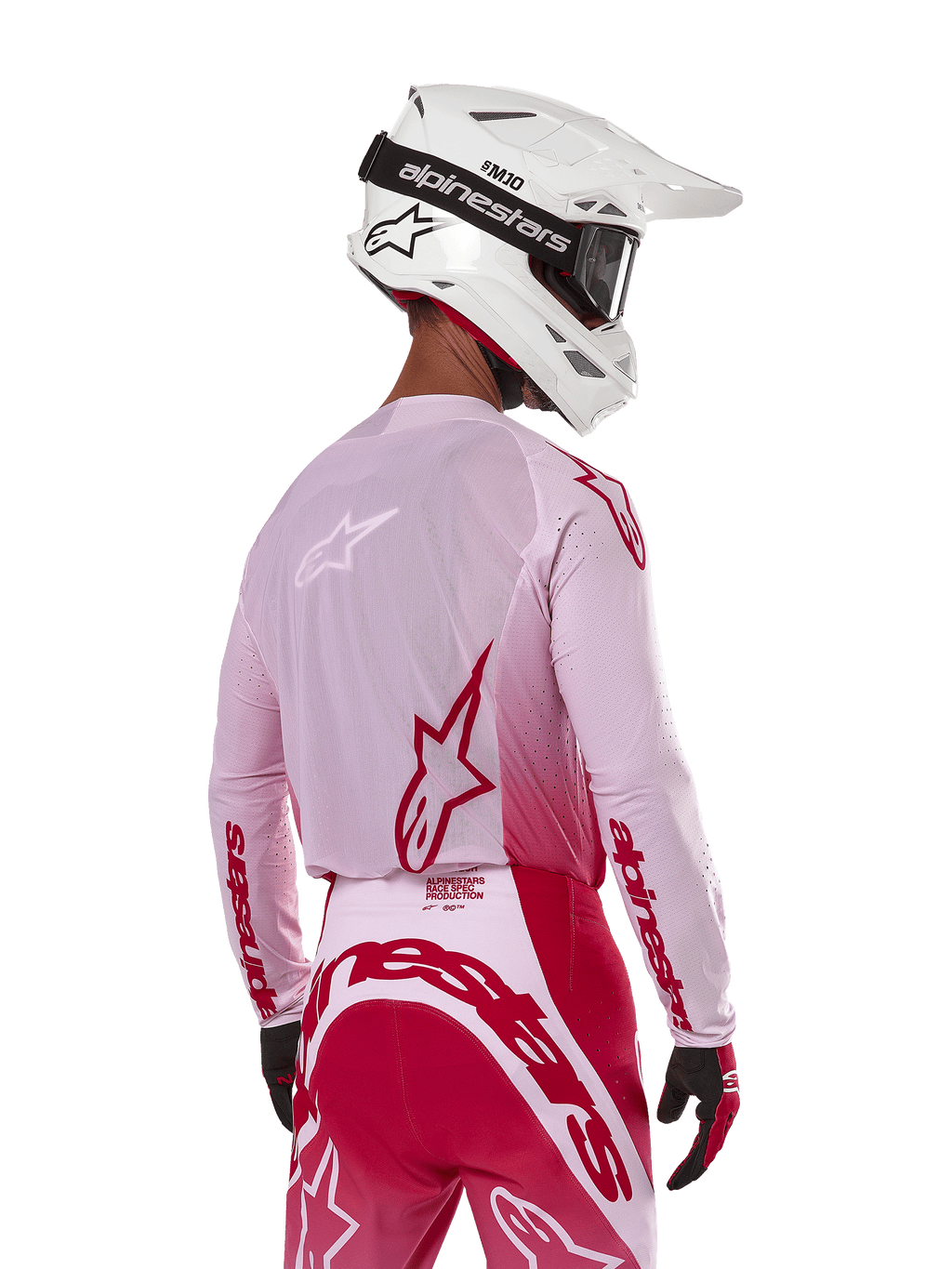 Motocyklista motocrossowy widziany od tyłu w koszulce Alpinestars 2024 Supertech Dade w kolorze Red Berry Lilac, z oddychającymi panelami z siatki i czerwonymi logo Alpinestars, w zestawie z pasującymi czerwono-liliowymi spodniami oraz białym kaskiem Alpinestars z goglami, profesjonalny sprzęt do wyścigów off-road