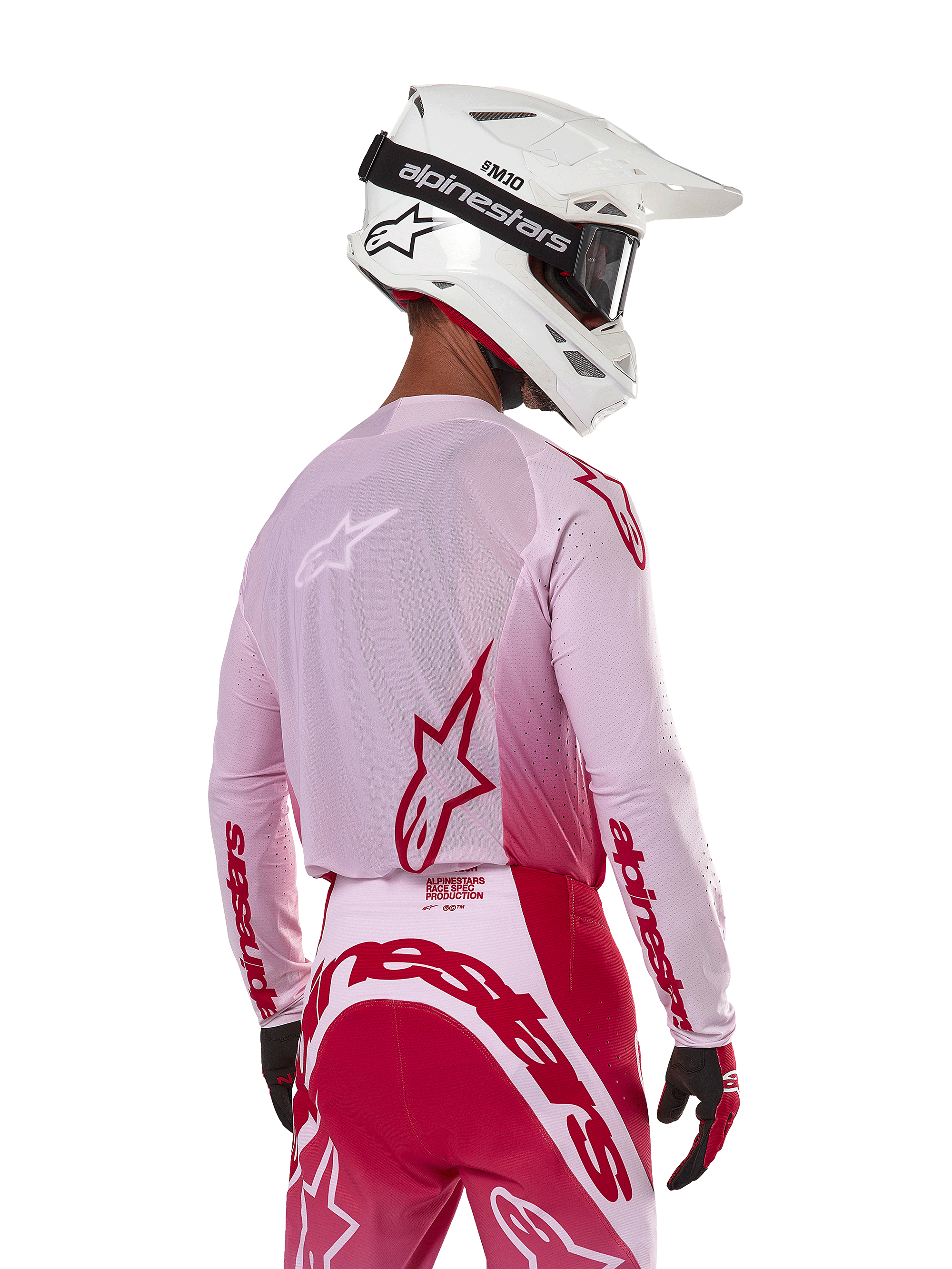 Motocyklista motocrossowy widziany od tyłu w koszulce Alpinestars 2024 Supertech Dade w kolorze Red Berry Lilac, z oddychającymi panelami z siatki i czerwonymi logo Alpinestars, w zestawie z pasującymi czerwono-liliowymi spodniami oraz białym kaskiem Alpinestars z goglami, profesjonalny sprzęt do wyścigów off-road