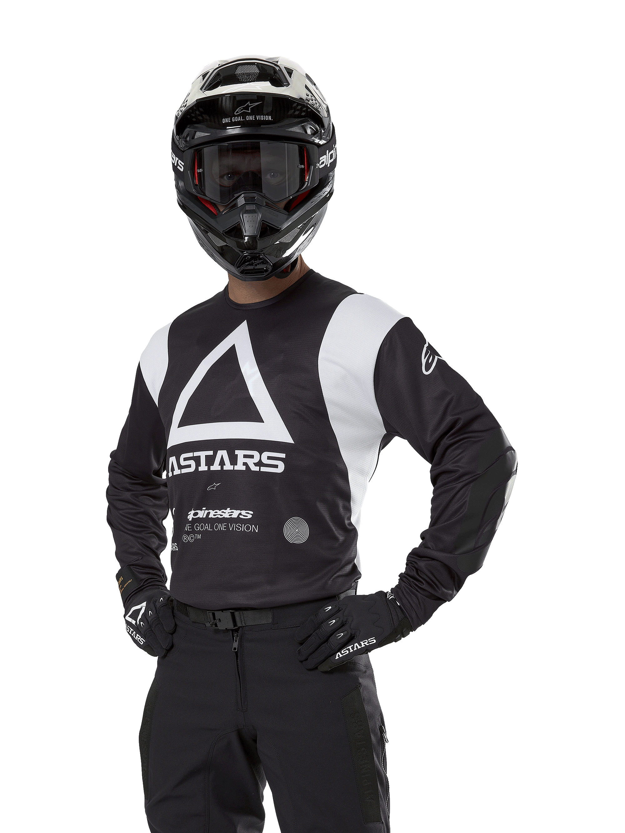 Alpinestars Techdura Jersey, koszulka motocrossowa, czarno-biała, noszona z pasującym kaskiem i rękawicami, poza z rękami na biodrach na białym tle, z dużym trójkątnym logo A i brandingiem ASTARS