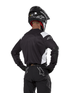 Alpinestars Techdura Jersey, czarna z białymi akcentami na ramionach, widok z tyłu na motocyklistę w pasujących czarnych spodniach i kasku, wzmocnione łaty na łokciach, odzież do enduro i jazdy terenowej