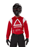 Kierowca motocrossowy w koszulce Alpinestars Techdura Jersey, jasnoczerwona z białą grafiką, duży biały trójkąt i logo ASTARS na klatce piersiowej, czarny kask, czarne gogle i czarny strój, zestaw do jazdy enduro i off-road