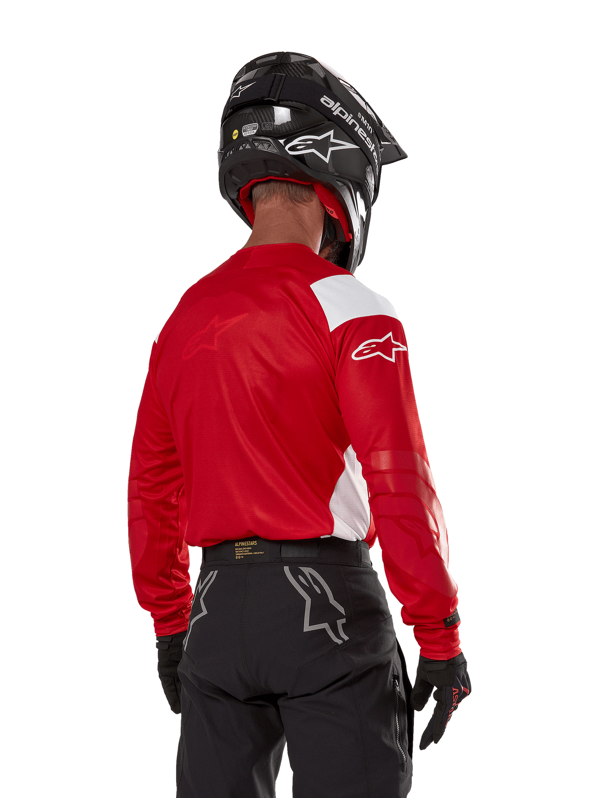 Motocyklista motocrossowy widziany od tyłu w koszulce Alpinestars Techdura w kolorze jasnoczerwonym z białymi panelami, zestawionej z czarnymi spodniami off-road, czarnym kaskiem i czarnymi rękawicami; dopasowany zestaw odzieży do jazdy enduro i motocrossowej.