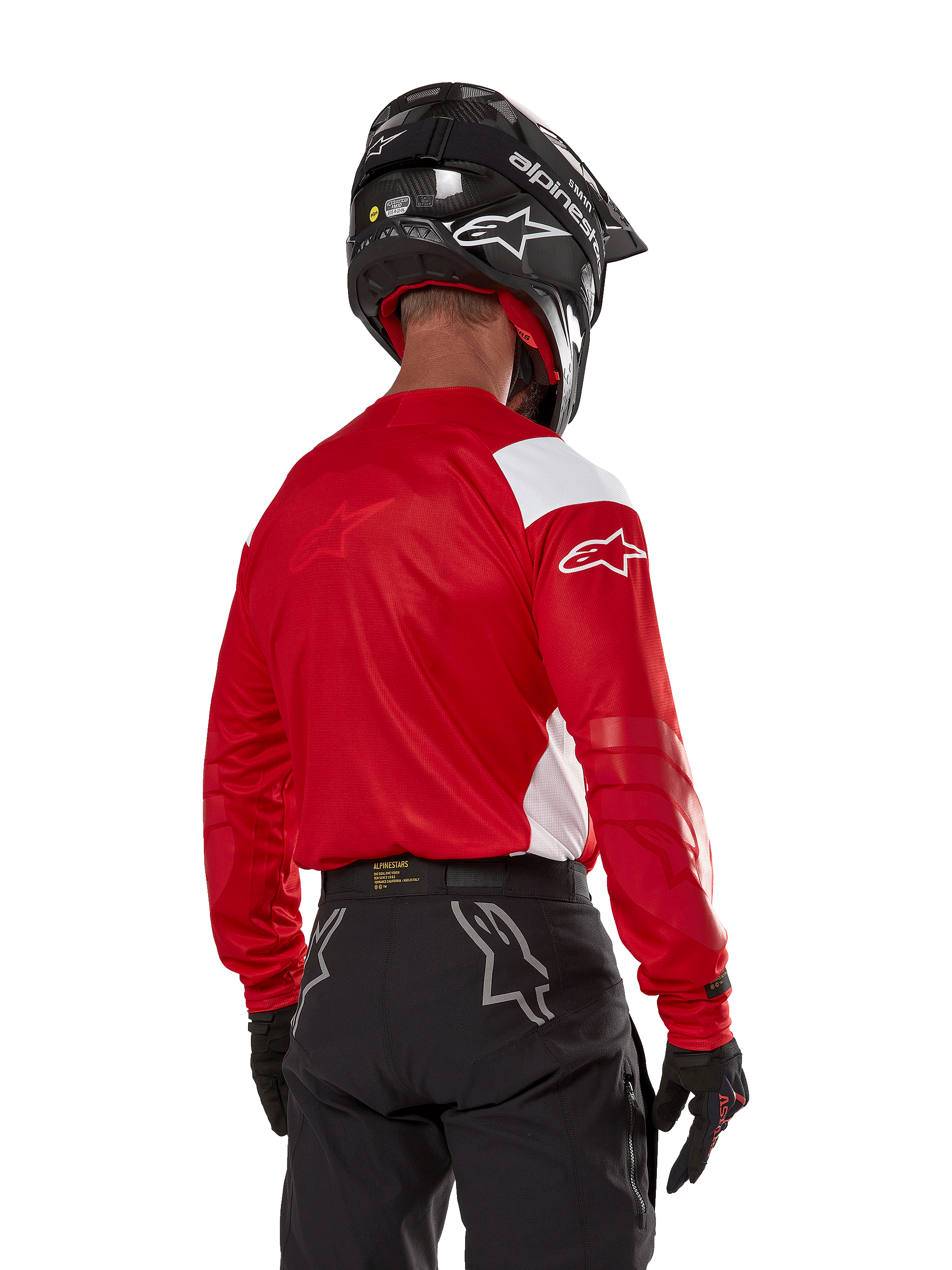 Motocyklista motocrossowy widziany od tyłu w koszulce Alpinestars Techdura w kolorze jasnoczerwonym z białymi panelami, zestawionej z czarnymi spodniami off-road, czarnym kaskiem i czarnymi rękawicami; dopasowany zestaw odzieży do jazdy enduro i motocrossowej.