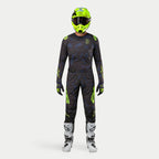Kierowca motocrossowy w pełnym stroju wyścigowym, koszulka Techstar Rantera 2024 w kolorze Black Navy i Yellow Fluo, dopasowane spodnie z abstrakcyjnym nadrukiem, jaskrawy kask w kolorze żółty fluo, biało-czarne buty, skoordynowany zestaw do wyścigów terenowych