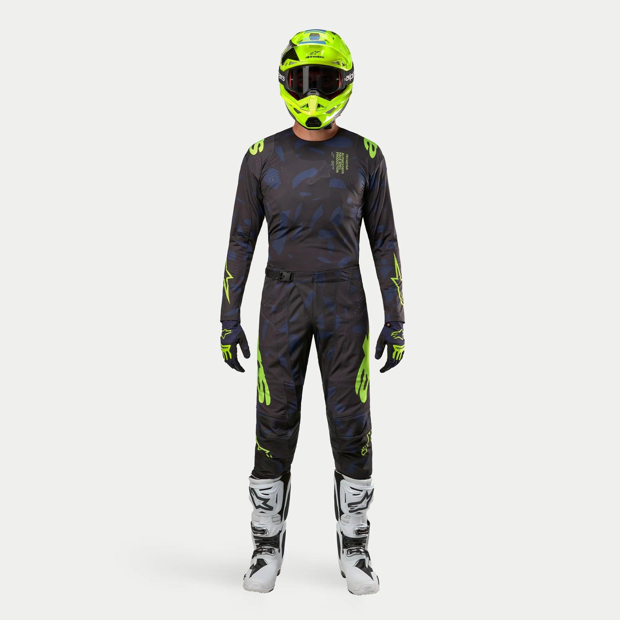 Kierowca motocrossowy w pełnym stroju wyścigowym, koszulka Techstar Rantera 2024 w kolorze Black Navy i Yellow Fluo, dopasowane spodnie z abstrakcyjnym nadrukiem, jaskrawy kask w kolorze żółty fluo, biało-czarne buty, skoordynowany zestaw do wyścigów terenowych