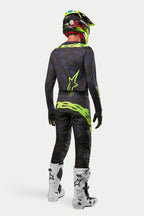Alpinestars 2024 Techstar Rantera Jersey i spodnie, zawodnik motocrossowy w pełnym rynsztunku widziany od tyłu, kolor czarny, granatowy i żółty fluorescencyjny, pasujący żółty kask fluo i białe buty, skoordynowany zestaw do wyścigów off-road