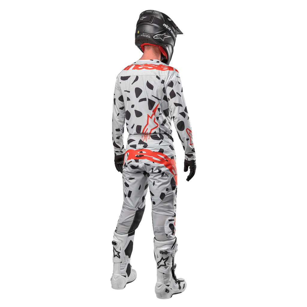 Motocyklista motocrossowy widoczny od tyłu w koszulce Alpinestars 2024 Techstar Rantera i pasujących spodniach, wzór Haze Gray Camo z wyraźnymi czerwonymi logo Alpinestars, czarny kask, biało-czarne buty, czarne rękawice, dopasowany komplet odzieży motocrossowej