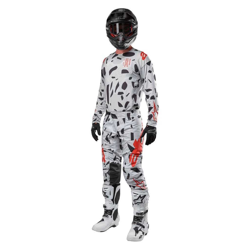 Zawodnik motocrossowy w koszulce Alpinestars 2024 Techstar Rantera w kolorze Haze Gray Camo, pasujące spodnie z czerwonymi i czarnymi akcentami, czarny kask i gogle, czarne rękawice, biało-czarne buty, kompletny, skoordynowany zestaw wyścigowy motocross do jazdy terenowej
