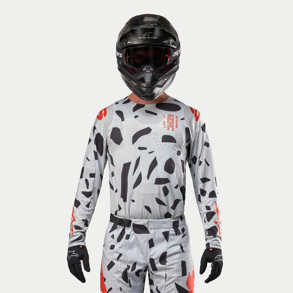 Alpinestars Techstar Rantera Jersey 2024, koszulka motocrossowa, Haze Gray Camo z czarnymi nieregularnymi wzorami i czerwonymi akcentami, noszona przez zawodnika z pasującymi spodniami, czarnym kaskiem i rękawicami, sportowa odzież terenowa