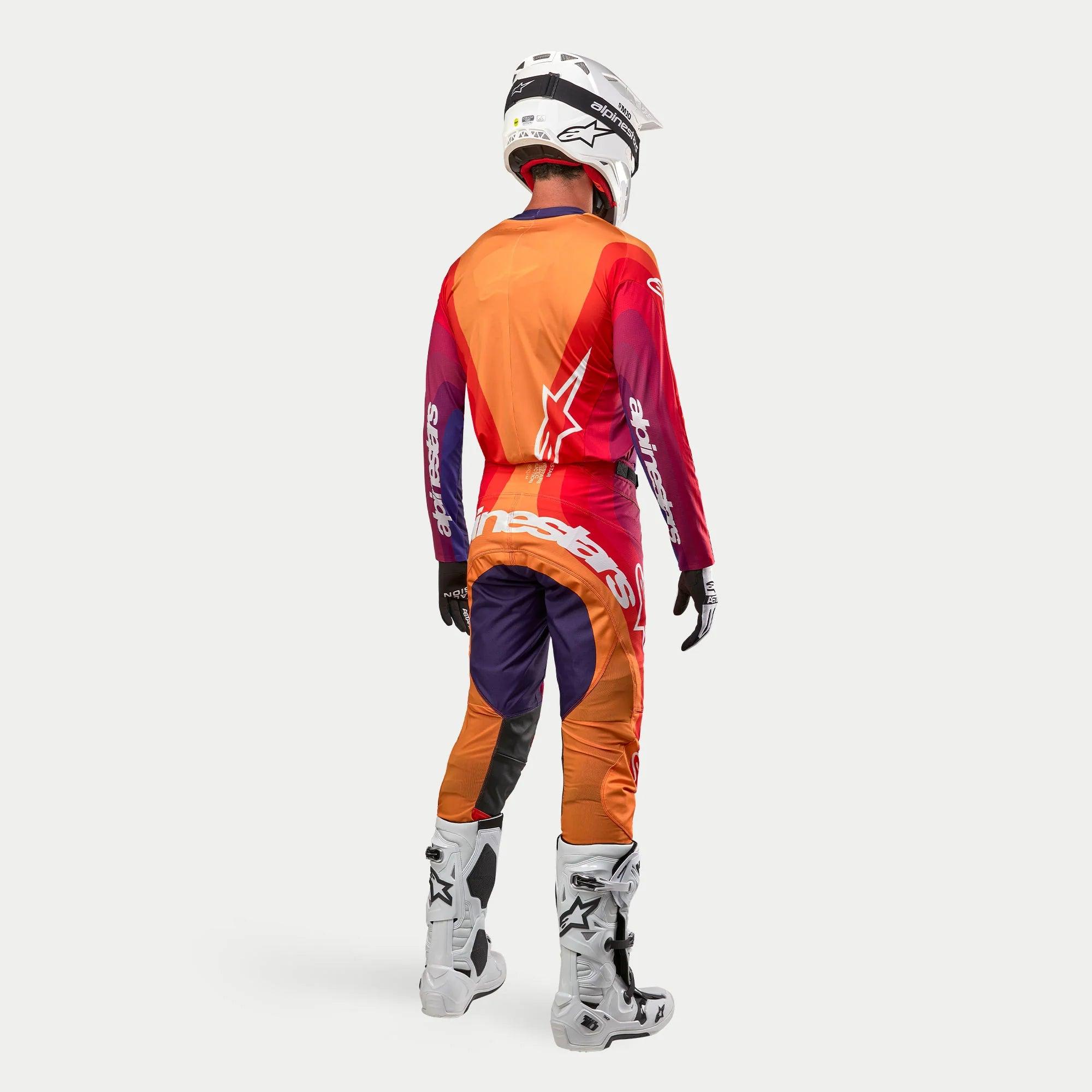 Alpinestars Techstar Pneuma 2024, kompletny strój motocrossowy widziany od tyłu, fioletowy, pomarańczowy i niebieski z białymi logotypami, biały kask, białe buty off-road, sportowy krój wyścigowy
