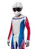 Alpinestars Techstar Pneuma Jersey 2024, bluza motocrossowa, niebiesko-czerwono-biała z fioletowymi akcentami, sportowy krój wyścigowy, techniczna odzież z długim rękawem prezentowana z białym kaskiem i rękawicami