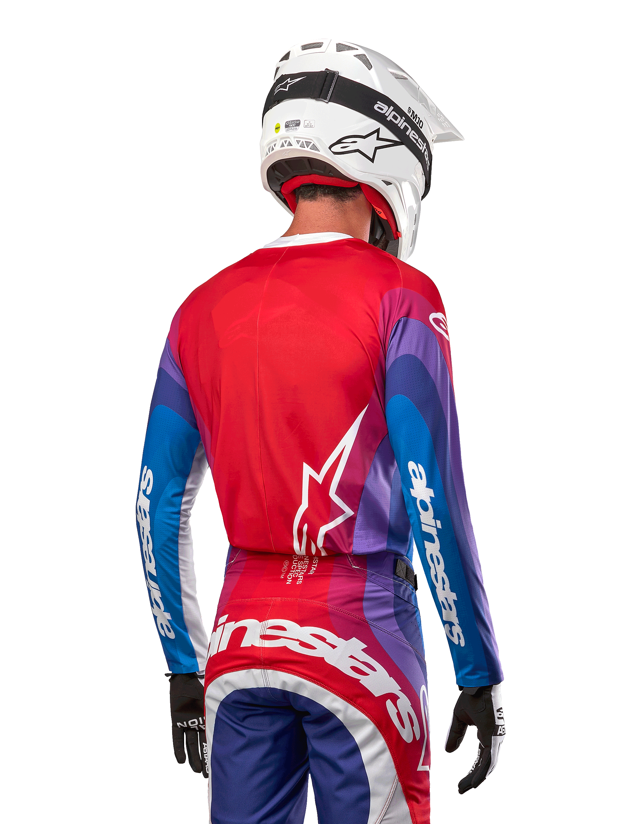 Zawodnik motocrossowy od tyłu w koszulce Alpinestars 2024 Techstar Pneuma w kolorze Blue Mars Red White, czerwony tył z białym logo gwiazdy, niebieskie i fioletowe rękawy z białym brandingiem, w komplecie z pasującymi spodniami i białym kaskiem do jazdy terenowej.