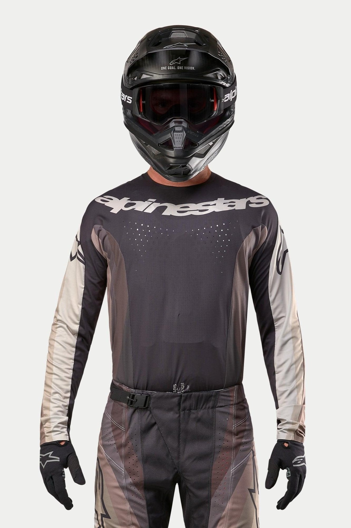 Koszulka Alpinestars Techstar Pneuma 2024, koszulka motocrossowa w kolorach Dark Sand i Iron Dust Gray, zestawiona z pasującymi spodniami motocrossowymi i czarnym kaskiem, z widocznym logo Alpinestars na klatce piersiowej i laserowo wycinaną perforacją wentylacyjną, profesjonalna odzież do wyścigów off-road.