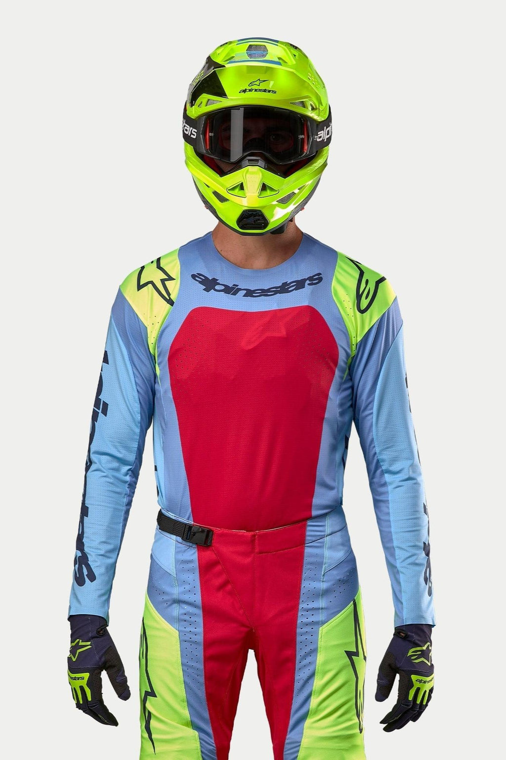 Motocrossista w pełnym stroju wyścigowym, koszulka Techstar Ocuri 2024 w jasnoniebieskim kolorze z dużym czerwonym panelem na klatce piersiowej i żółtymi akcentami fluo na ramionach, dopasowany neonowy żółty kask, pasujące czerwone i żółte spodnie fluo, profesjonalny strój do wyścigów terenowych