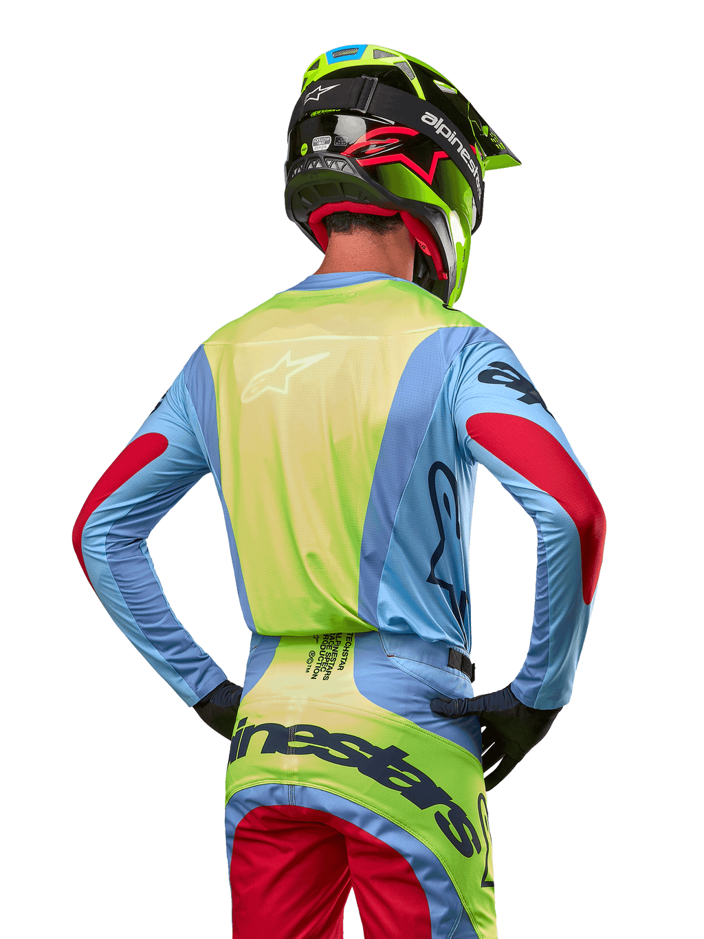 Motocyklista motocrossowy widoczny od tyłu w koszulce Alpinestars 2024 Techstar Ocuri, jasnoniebieska z neonowożółtym tyłem i czerwonymi akcentami na rękawach, dopasowane spodnie motocrossowe i neonowożółty kask, skoordynowany strój do wyścigów terenowych