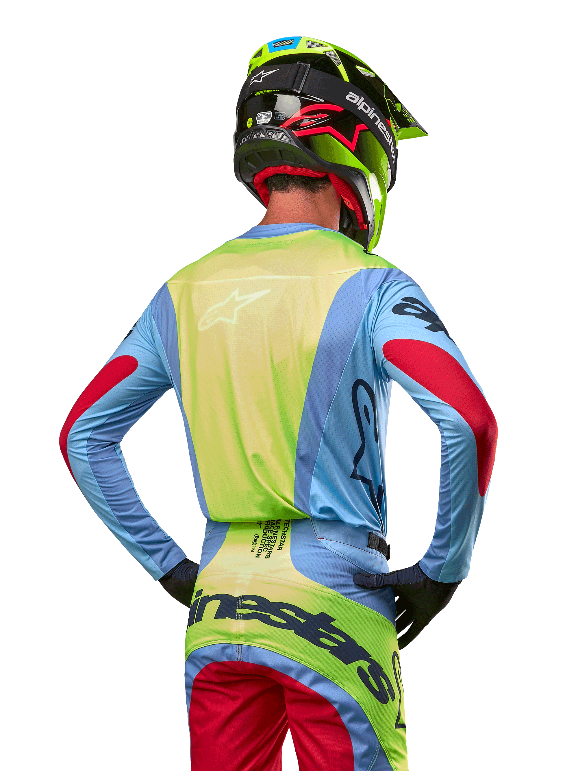 Motocyklista motocrossowy widoczny od tyłu w koszulce Alpinestars 2024 Techstar Ocuri, jasnoniebieska z neonowożółtym tyłem i czerwonymi akcentami na rękawach, dopasowane spodnie motocrossowe i neonowożółty kask, skoordynowany strój do wyścigów terenowych