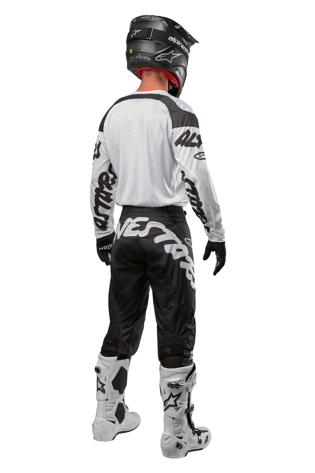 Alpinestars 2024 Racer Hana Jersey, widok z tyłu na zawodnika motocrossowego, biało-czarna, biała koszulka z czarnymi grafikami na rękawach, czarne spodnie z białym napisem Alpinestars na siedzeniu, czarny kask oraz biało-czarne buty, dopasowany strój do wyścigów terenowych