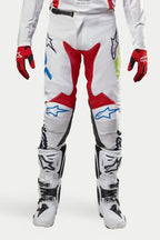Alpinestars 2024 Racer Hana Pants, spodnie motocrossowe, białe z czerwonymi, niebieskimi i limonkowymi akcentami, zestawione z biało-czarnymi butami i czerwonymi rękawicami, logo Alpinestars na kolanach, wytrzymała techniczna konstrukcja do jazdy terenowej