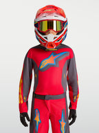 Koszulka Alpinestars Youth Fluid Hunt 2027, młodzieżowa odzież MX, czerwona i szara, model w kasku wyścigowym.