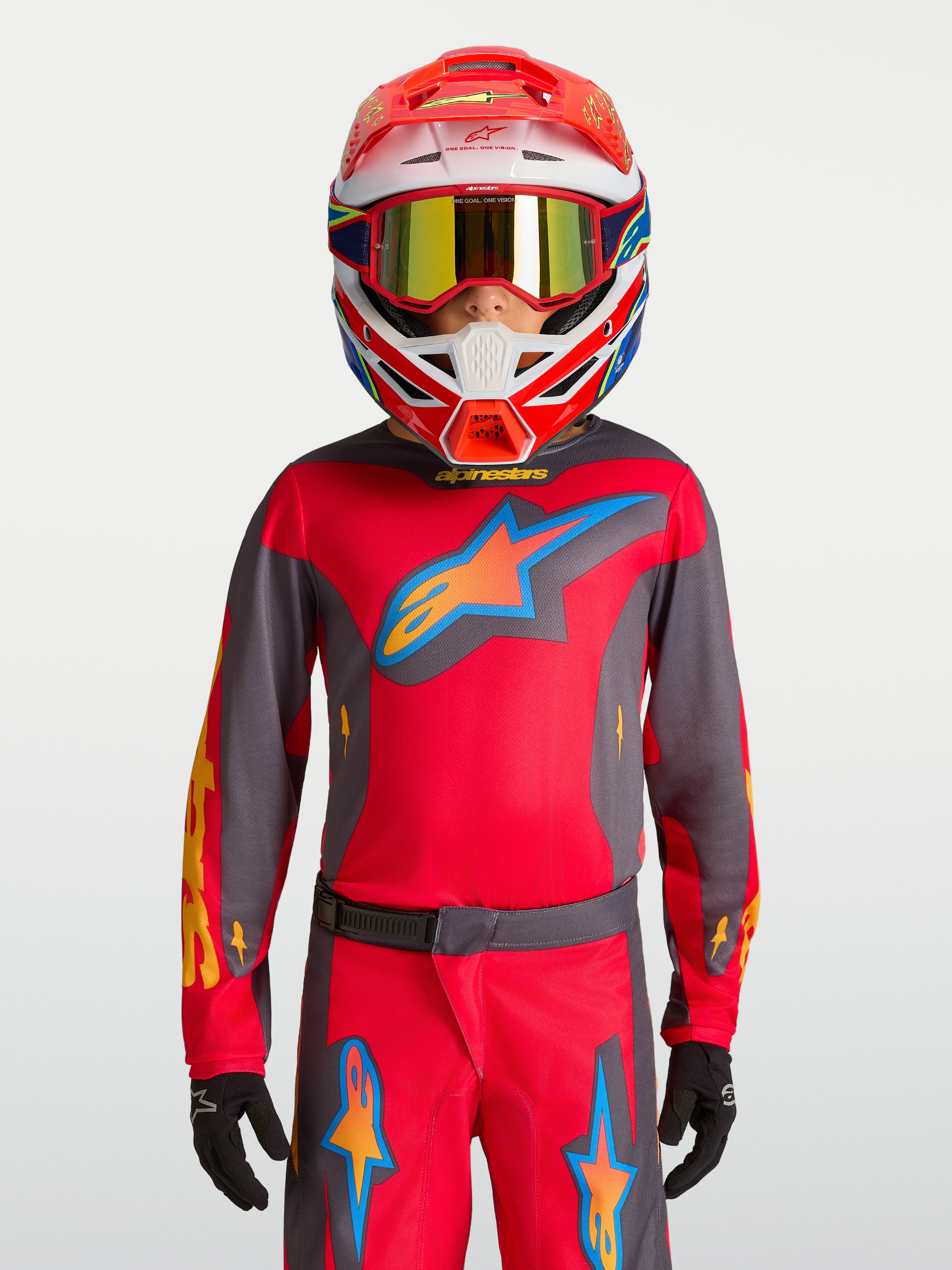 Koszulka Alpinestars Youth Fluid Hunt 2027, młodzieżowa odzież MX, czerwona i szara, model w kasku wyścigowym.