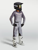 Młodzieżowy zestaw Alpinestars Youth Fluid Amber, szara koszulka i spodnie motocrossowe, białe buty i czarny kask.