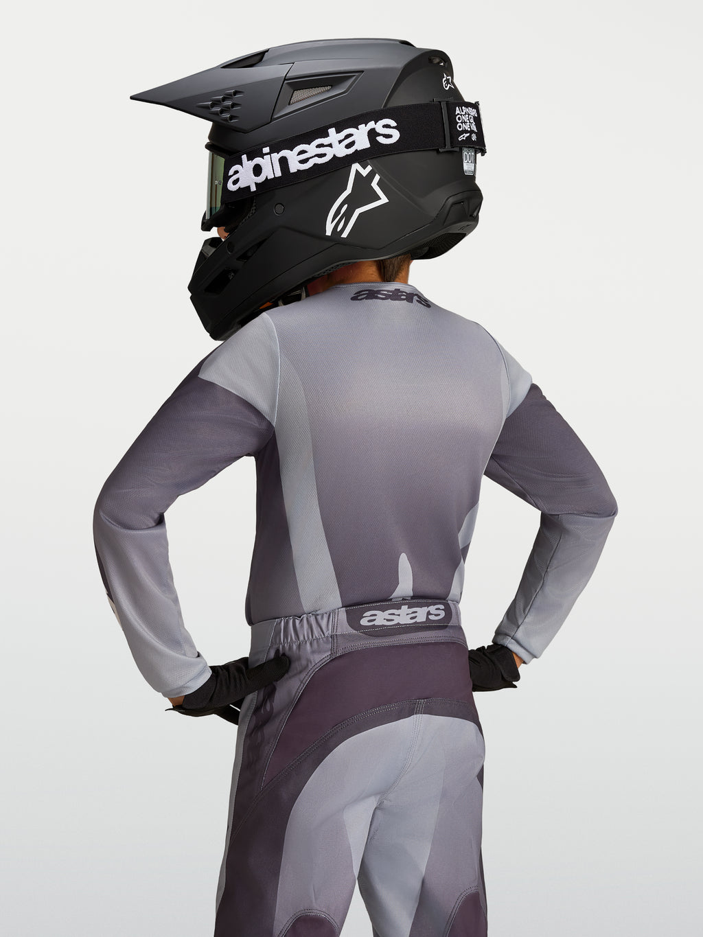 Alpinestars Koszulka Fluid Amber Młodzieżowe 2027, szara i piaskowa koszulka motocrossowa, widok z tyłu na młodym zawodniku.