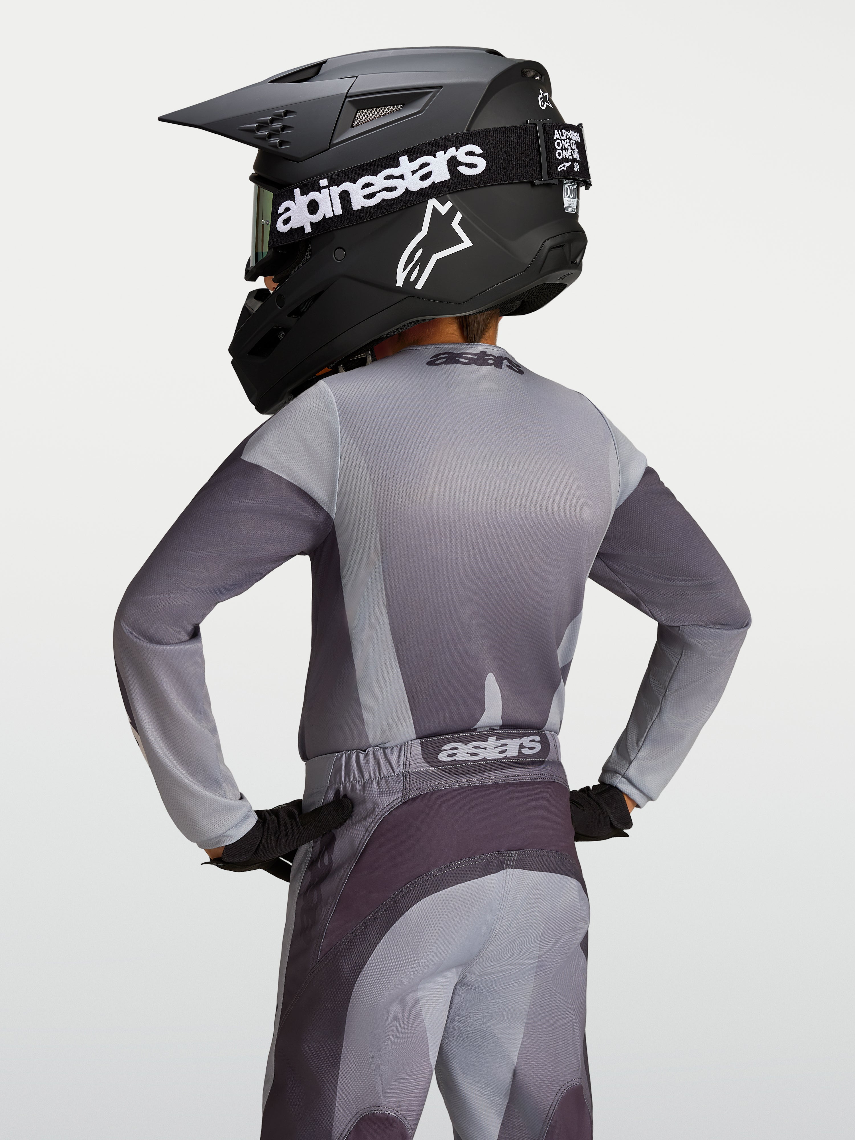 Alpinestars Koszulka Fluid Amber Młodzieżowe 2027, szara i piaskowa koszulka motocrossowa, widok z tyłu na młodym zawodniku.