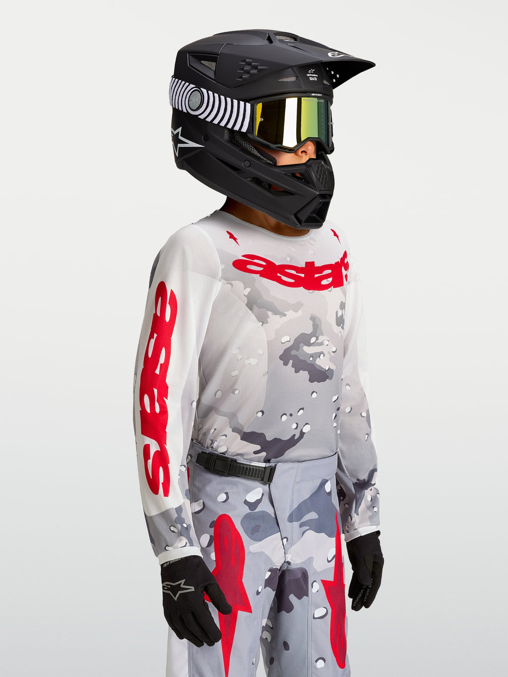 Alpinestars Fluid Lone Młodzieżowe 2027, koszulka motocrossowa, szary kamuflaż i kolor czerwony, model w kasku.