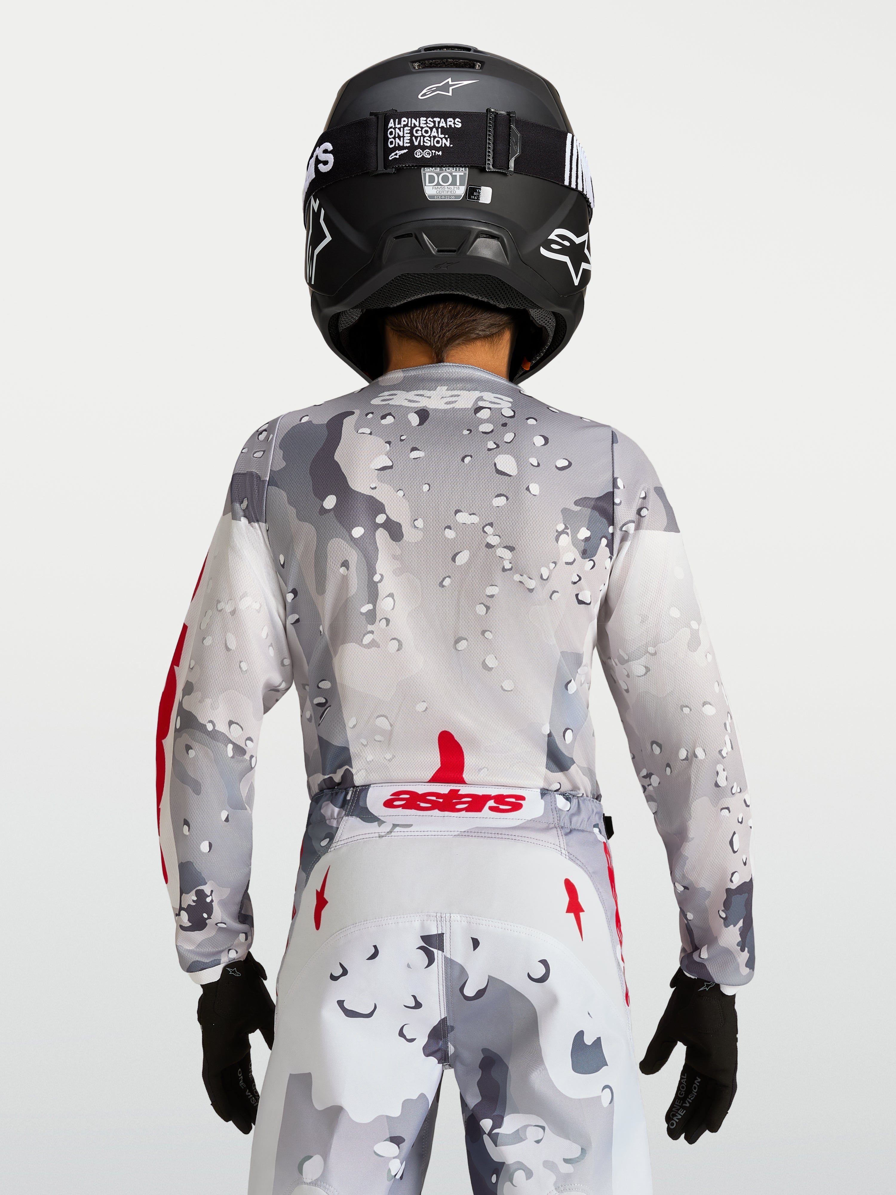 Alpinestars koszulka Fluid Lone Młodzieżowe 2027, szary kamuflaż, widok od tyłu, czerwone akcenty i czarny kask.