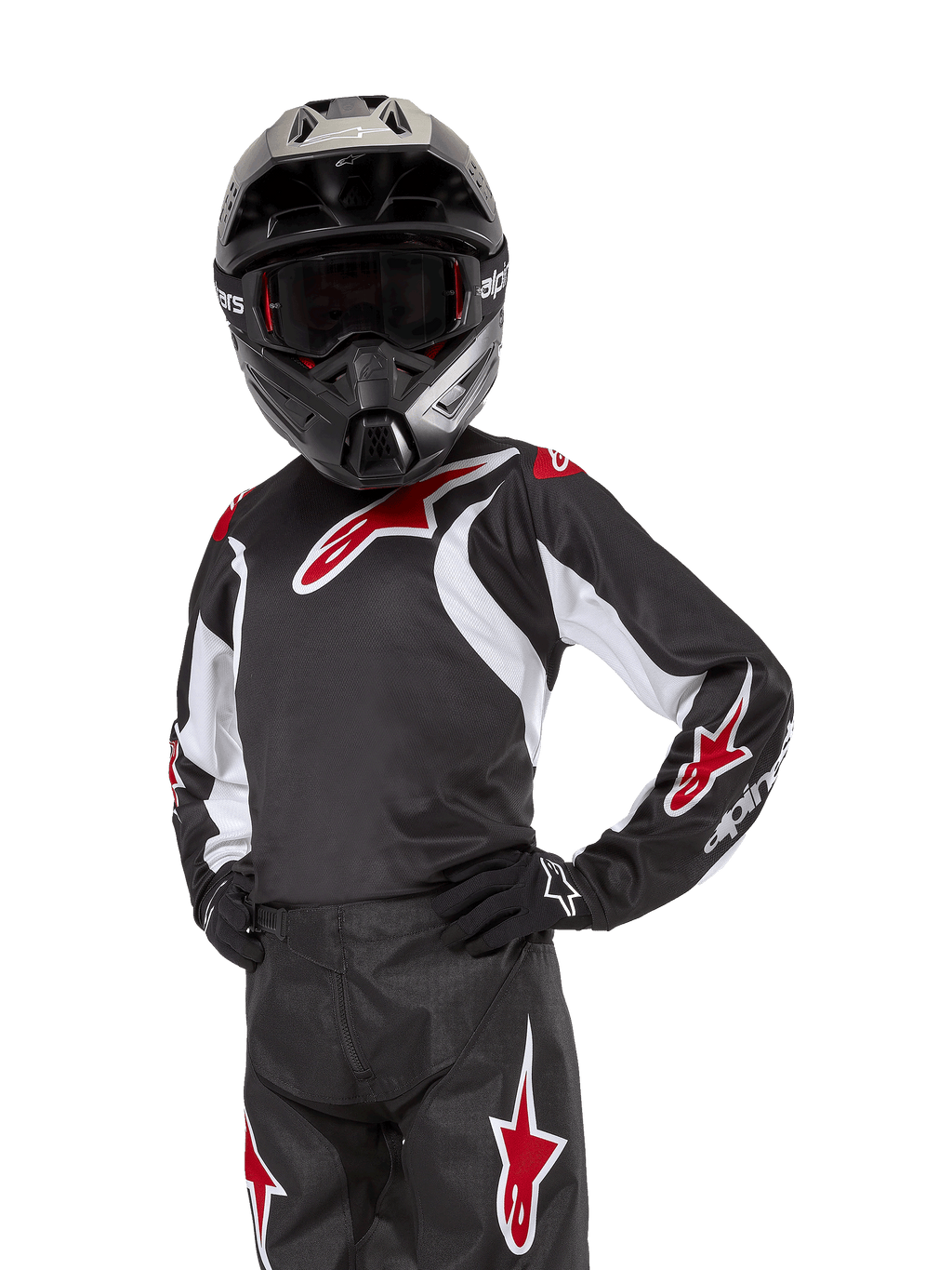 Alpinestars Youth 2024 Racer Lucent Jersey, młodzieżowa koszulka motocrossowa, czarno-biało-czerwona, noszona przez młodego zawodnika w czarnym kasku i pasujących spodniach, z czerwonymi logotypami gwiazdy i białymi akcentami graficznymi, wyczynowa odzież off-road