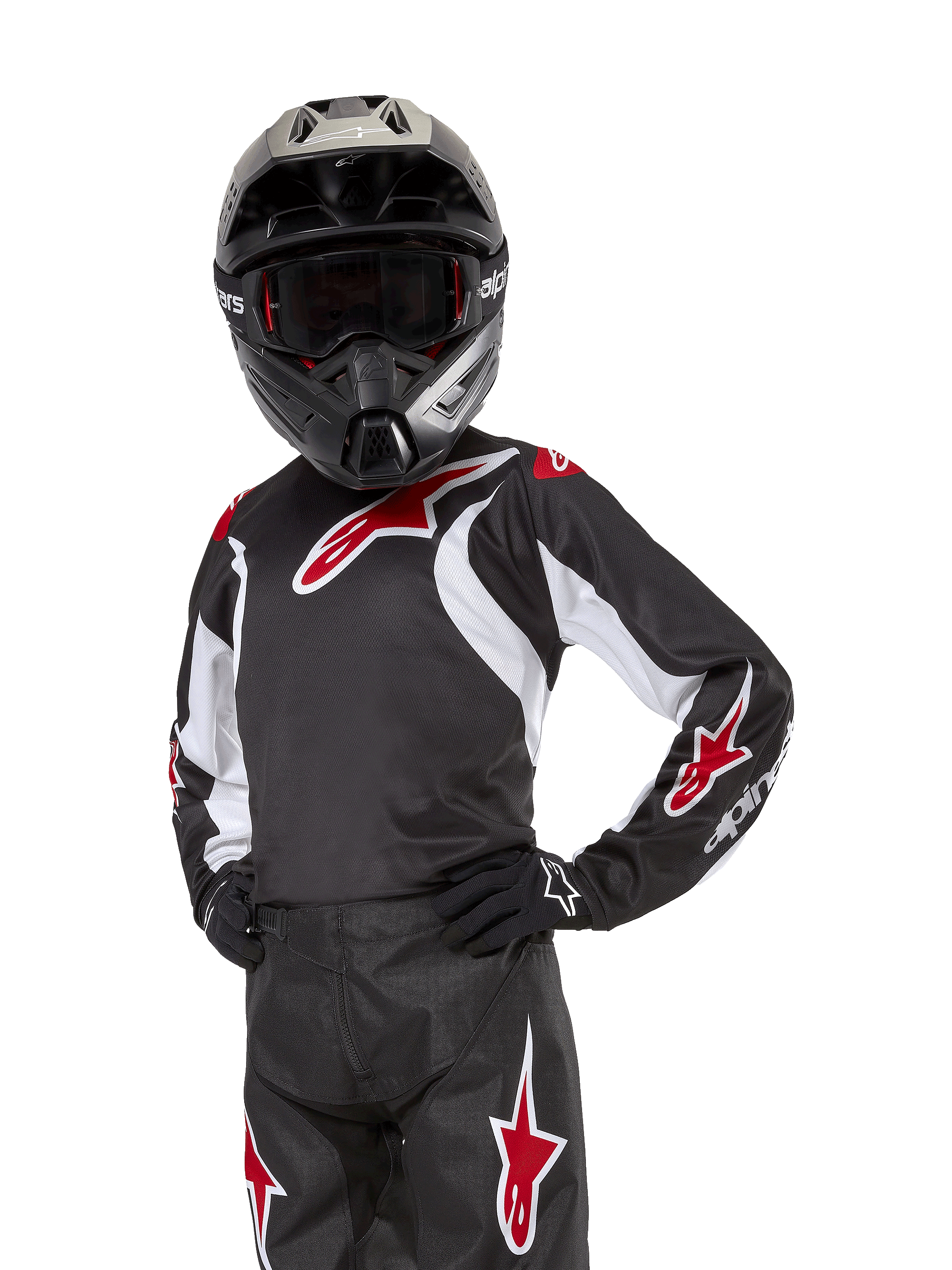 Alpinestars Youth 2024 Racer Lucent Jersey, młodzieżowa koszulka motocrossowa, czarno-biało-czerwona, noszona przez młodego zawodnika w czarnym kasku i pasujących spodniach, z czerwonymi logotypami gwiazdy i białymi akcentami graficznymi, wyczynowa odzież off-road