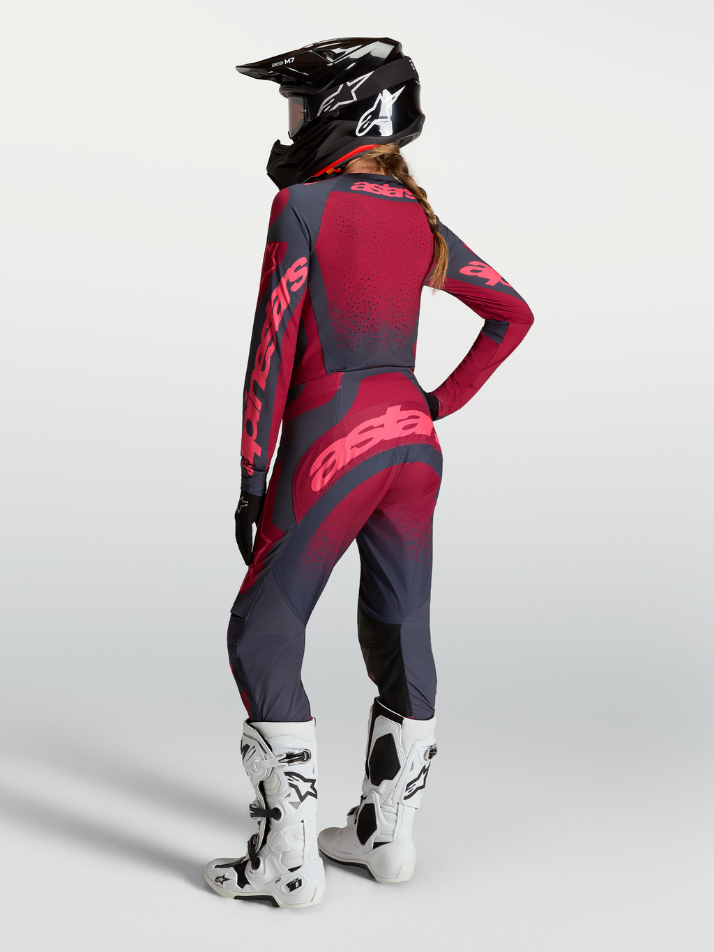 Alpinestars Stella Techstar Swan, damskie spodnie motocrossowe, czerwone i szare, elastyczna konstrukcja stretch, modelka w kasku i białych butach Tech 10, widok z tyłu