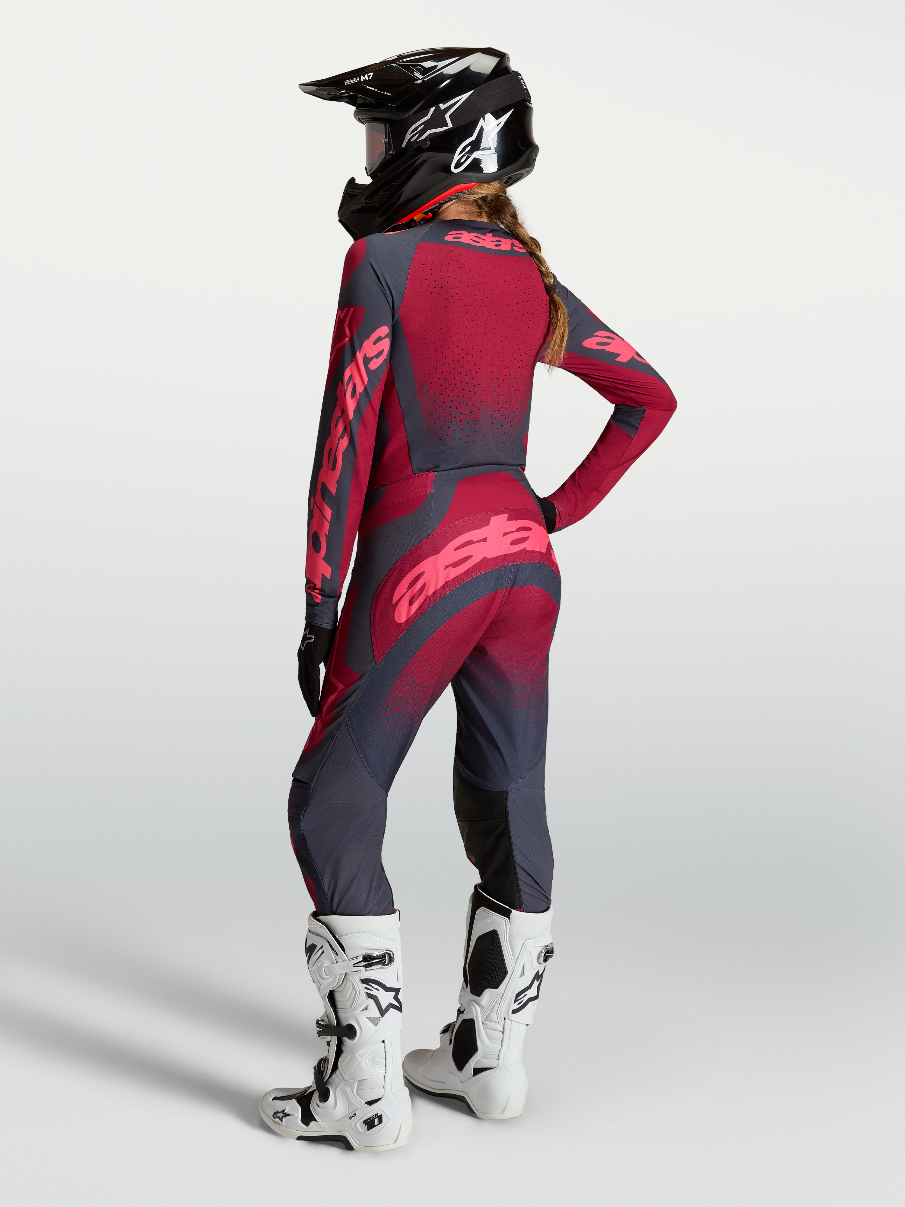 Alpinestars Stella Techstar Swan, damskie spodnie motocrossowe, czerwone i szare, elastyczna konstrukcja stretch, modelka w kasku i białych butach Tech 10, widok z tyłu