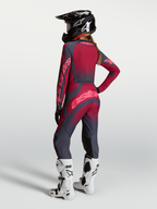 Alpinestars Koszulka Stella Techstar Swan i Stella Techstar Swan Gear Set, damski zestaw motocrossowy, czerwony i ciemnoszary, widok od tyłu na modelkę w kasku i białych butach.