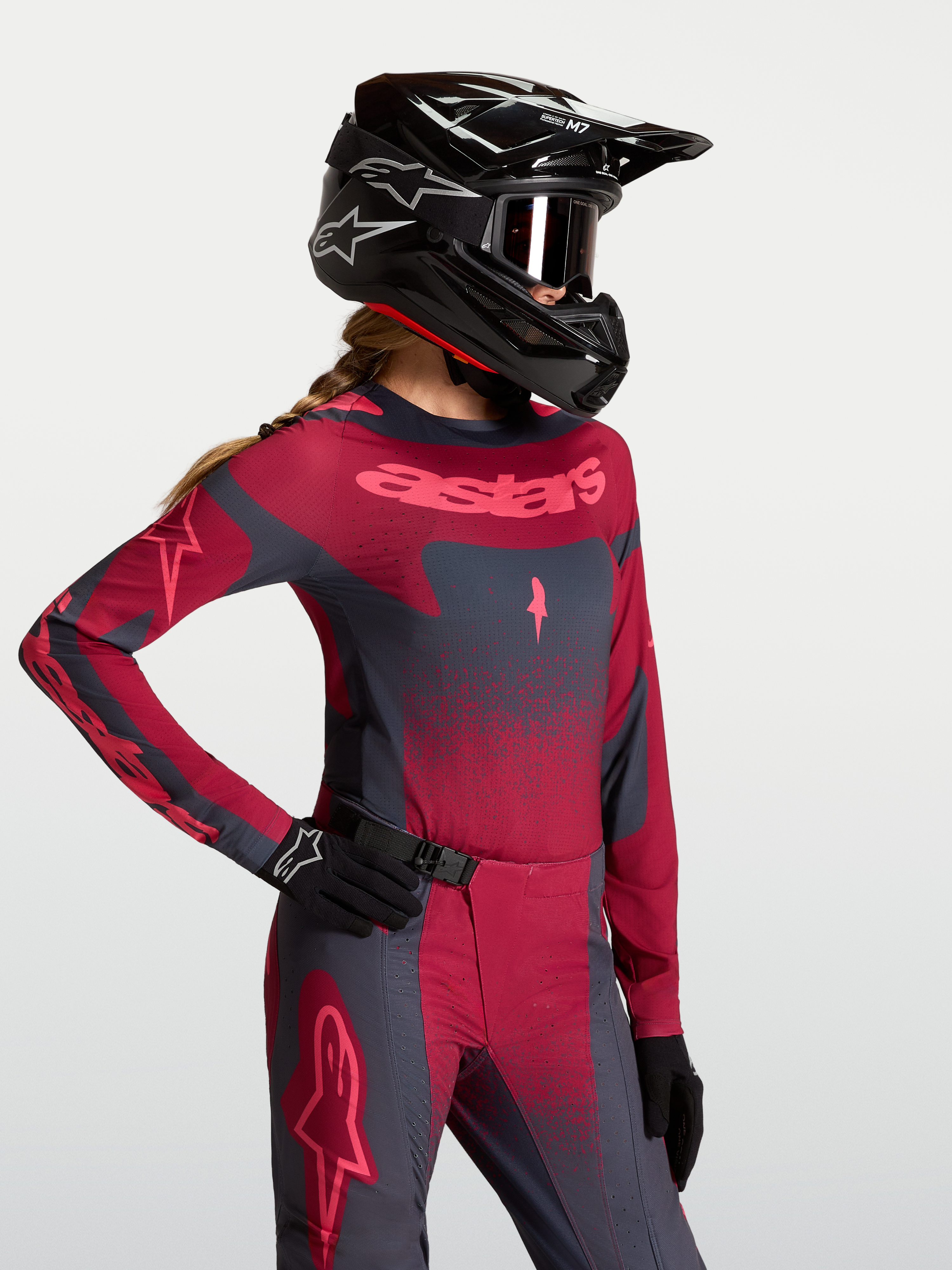 Alpinestars Koszulka Stella Techstar Swan, damska koszulka motocrossowa, ciemnoczerwona i ciemnoszara, sportowy krój wyścigowy, widoczna na modelu z kaskiem i rękawicami MX.