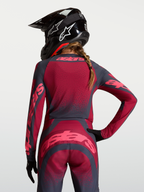 Alpinestars Stella Techstar Swan, koszulka motocrossowa damska, czerwona i ciemnoszara, elastyczny materiał z laserową wentylacją, widok od tyłu na kask i strój crossowy