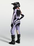 Alpinestars Stella Techstar Swan Jersey AND Stella Techstar Swan Gear Set, damska odzież motocrossowa, jasnofioletowa i czarna, widok od tyłu na modelkę w kasku i butach motocyklowych.