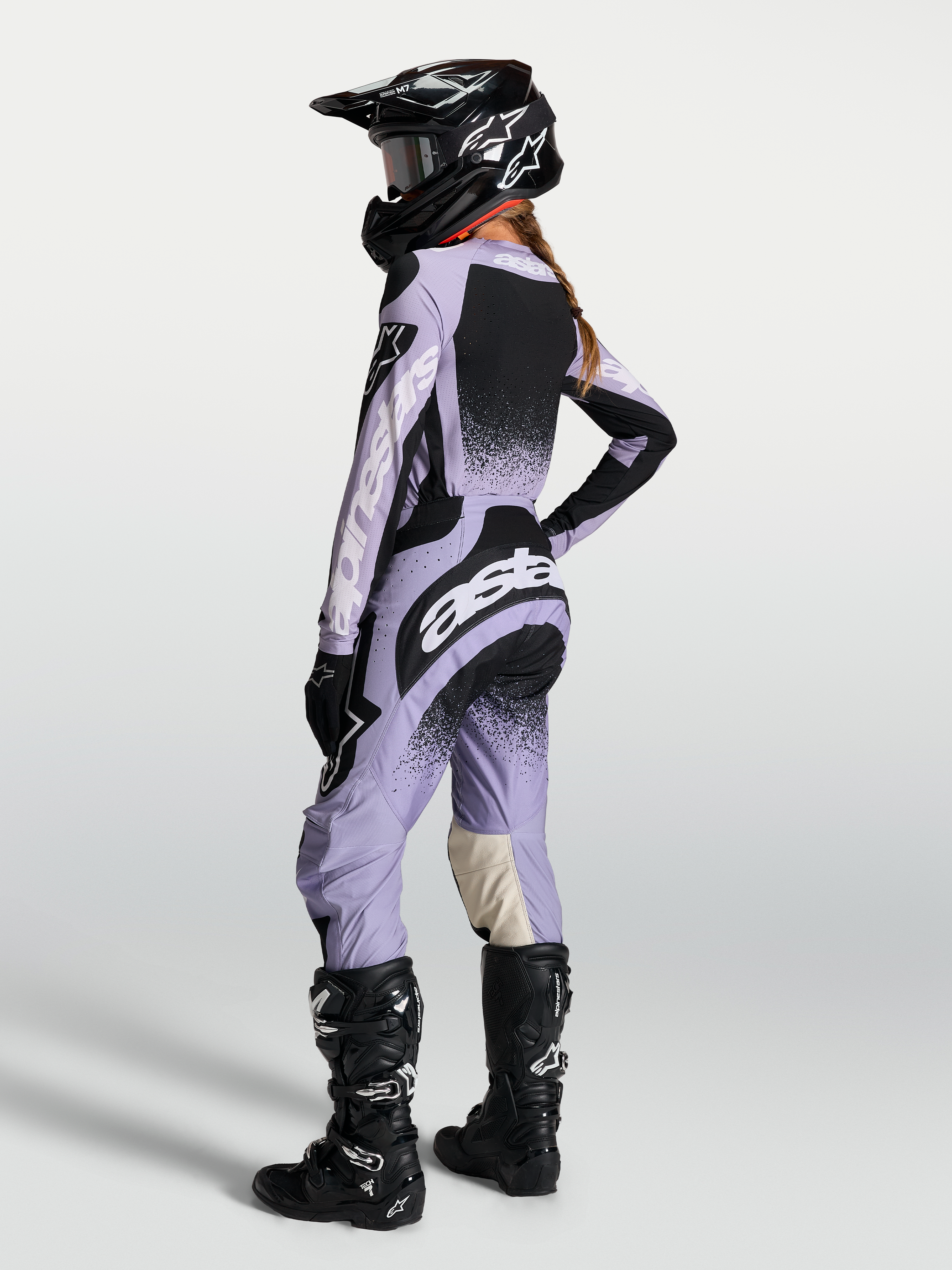 Alpinestars Stella Techstar Swan Jersey AND Stella Techstar Swan Gear Set, damska odzież motocrossowa, jasnofioletowa i czarna, widok od tyłu na modelkę w kasku i butach motocyklowych.