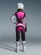 Alpinestars Stella Techstar Nomur Gear Set 2026, zawodniczka motocrossowa widoczna od tyłu, różowo-czarna koszulka z nakrapianym wzorem i pasiastymi rękawami, pasujące spodnie z białym logo, biały kask i białe buty off-road
