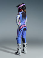 Alpinestars 2026 Stella Techstar Nomur Gear Set, widok z tyłu na zawodniczkę motocrossową w jasnoniebieskim, białym i różowym stroju z czarnymi nakrapianymi detalami, czarny kask i białe buty, profesjonalny zestaw wyścigowy dla kobiet