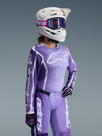 Damski zestaw Alpinestars 2026 Stella Fluid Apex, fioletowa i lawendowa bluza oraz spodnie motocrossowe, noszone przez zawodniczkę w białym kasku i fioletowych goglach, z wyraźnym białym brandingiem i logo Alpinestars