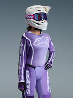 Zawodniczka motocrossowa w zestawie Alpinestars 2026 Stella Fluid Apex, fioletowo-biała bluza z logo Alpinestars, pasujące fioletowe spodnie, biały kask z fioletowymi goglami oraz czarno-fioletowe rękawice, profesjonalny strój off-road