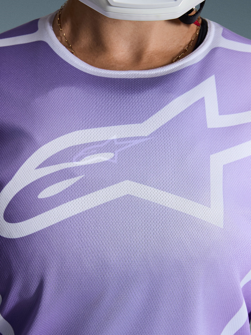 Koszulka Alpinestars Stella Fluid Apex 2026, zbliżenie na klatkę piersiową, fioletowa z białymi grafikami, duże białe logo Astars na siatkowej konstrukcji z poliestru