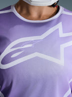 Koszulka Alpinestars Stella Fluid Apex 2026, zbliżenie na klatkę piersiową, fioletowa z białymi grafikami, duże białe logo Astars na siatkowej konstrukcji z poliestru