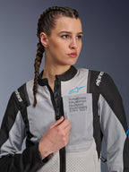 Kobieta w kurtce Alpinestars Stella ST-2 Air w kolorze Ice Gray i czarnym, portret z bliska, siatkowe panele wentylacyjne, branding „ALPINESTARS EXPLORATION EQUIPMENT” na klatce piersiowej z niebieskim logo, nowoczesna motocyklowa kurtka adventure