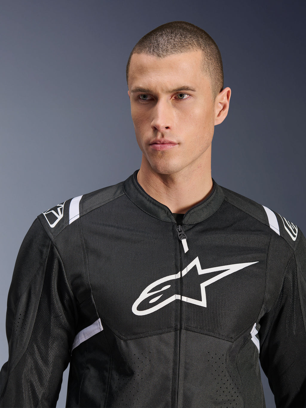 Kurtka Alpinestars T-SPS Air V2, tekstylna kurtka motocyklowa, czarno-biała, z dużym białym logo na klatce piersiowej i panelami z siatki, sportowy krój, prezentowana na modelu