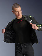Męski model ubrany w kurtkę Alpinestars T-Sps Air V2 w kolorze czarnym i żółtym fluo, rozpiętą, aby wyeksponować wewnętrzną konstrukcję z siatki i kieszenie, w zestawieniu z czarną warstwą bazową Alpinestars i czarnymi spodniami, miejski styl odzieży motocyklowej